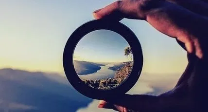 Hand holding lens showing a clear focused view of a mountain and lake