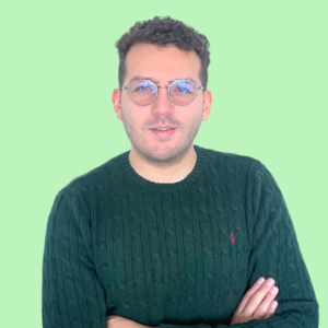 José Sebastián Torres wearing a dark green sweater and glasses, standing confidently against a light green background.