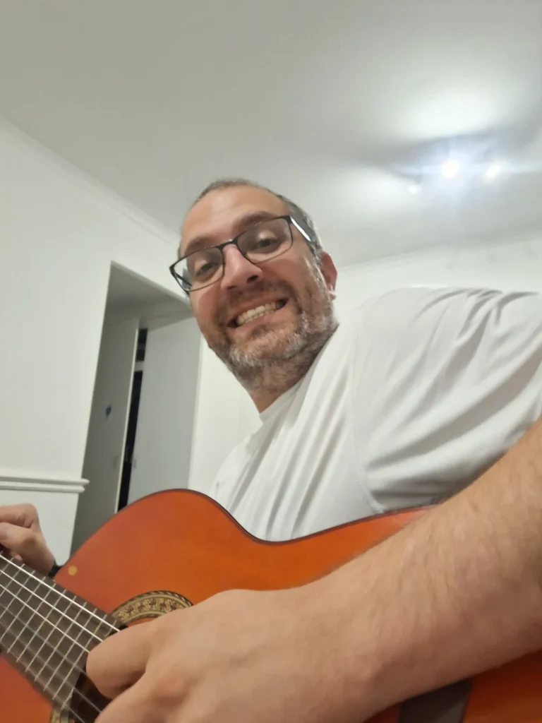 Elad Smadja smiling while playing acoustic guitar in a white t-shirt