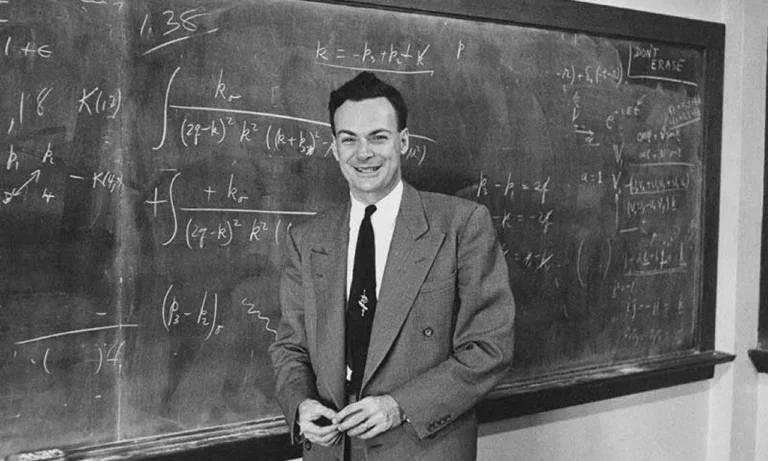 Richard Feynman smiling in front of a blackboard filled with mathematical formulas